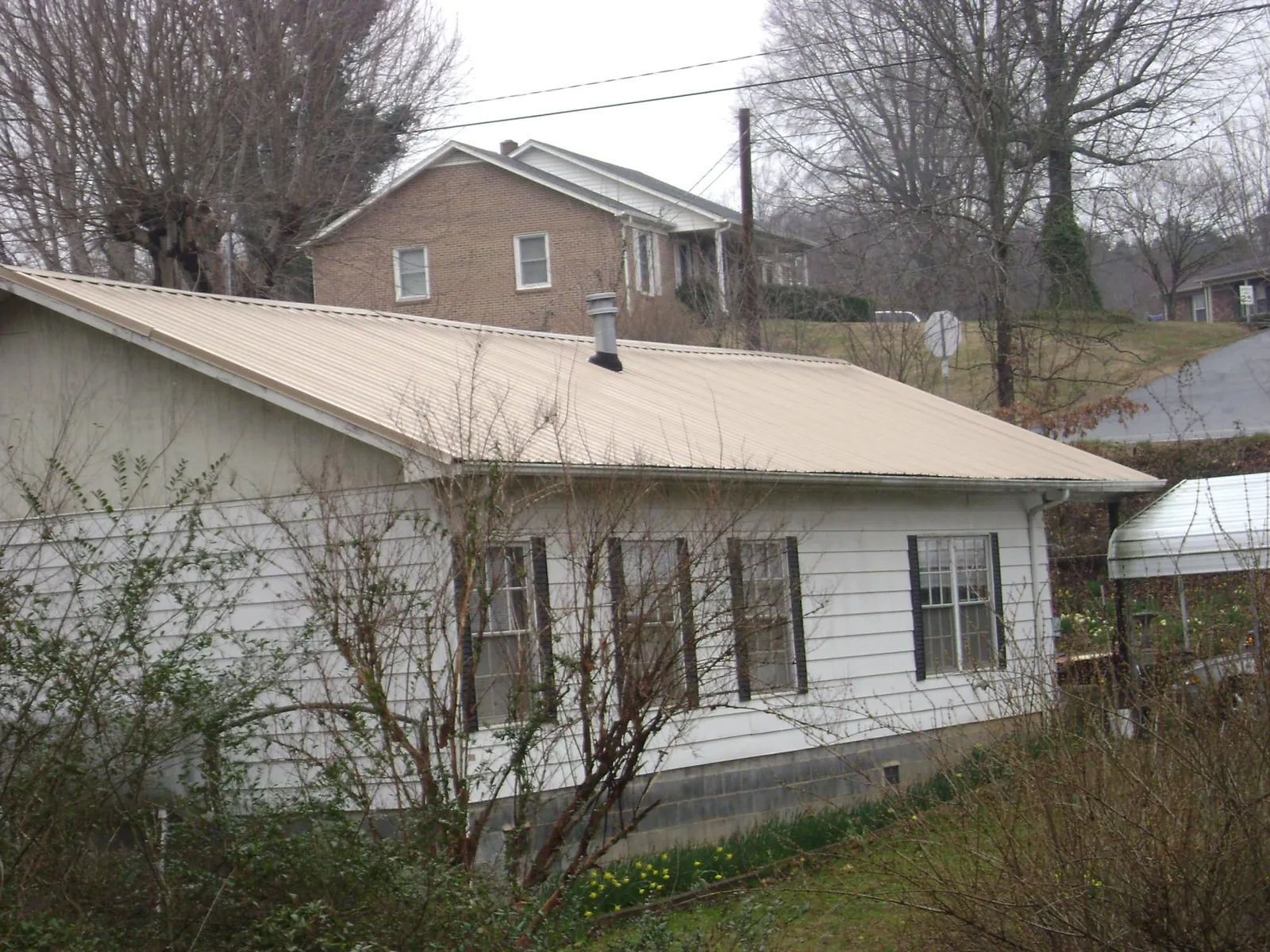 Tan metal roof on a white sided house set into a hillside — Commercial Roofing by Roofing Brothers in Roscoe